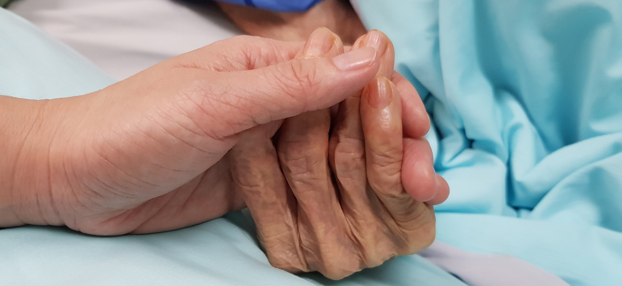 Woman-holding-mother’s-hand-in-hospice-care-and-receiving-bereavement-care